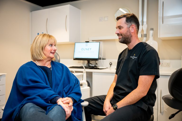 Dentist in a black gown consulting with a female patient with blonde hair and a blue sweater