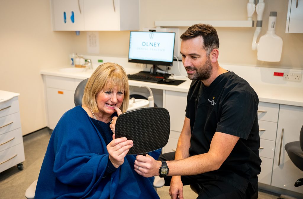 A dentist holding a mirror so that his patient can examine the work he has completed