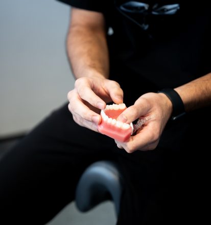 Dentist holding a model of a lower set of teeth and an Invisalign® strip